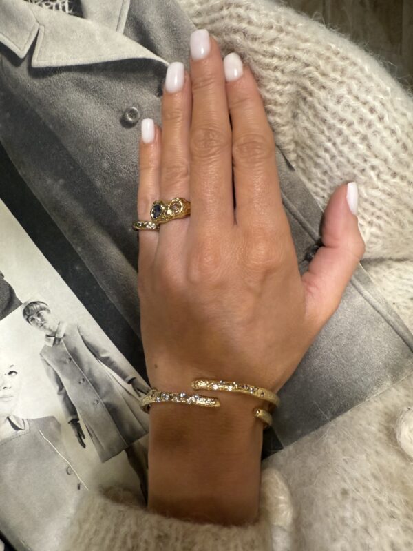 damska dłoń prezentująca dwa pierścionki i dwie bransoletki, tłem jest czarno- biała gazeta.